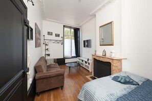 A modern room with a brown sofa, a small round table, a fireplace, and a bed with a patterned blanket. - The 17th historic heart of Nancy (Nancy)