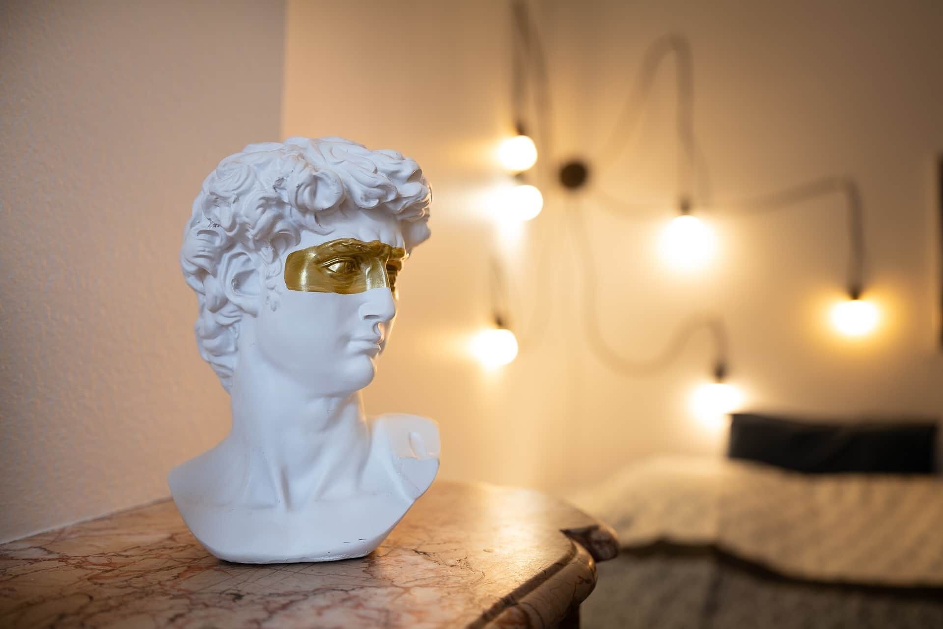 A bust sculpture on a marble surface with a blurred background of a bed and string lights.