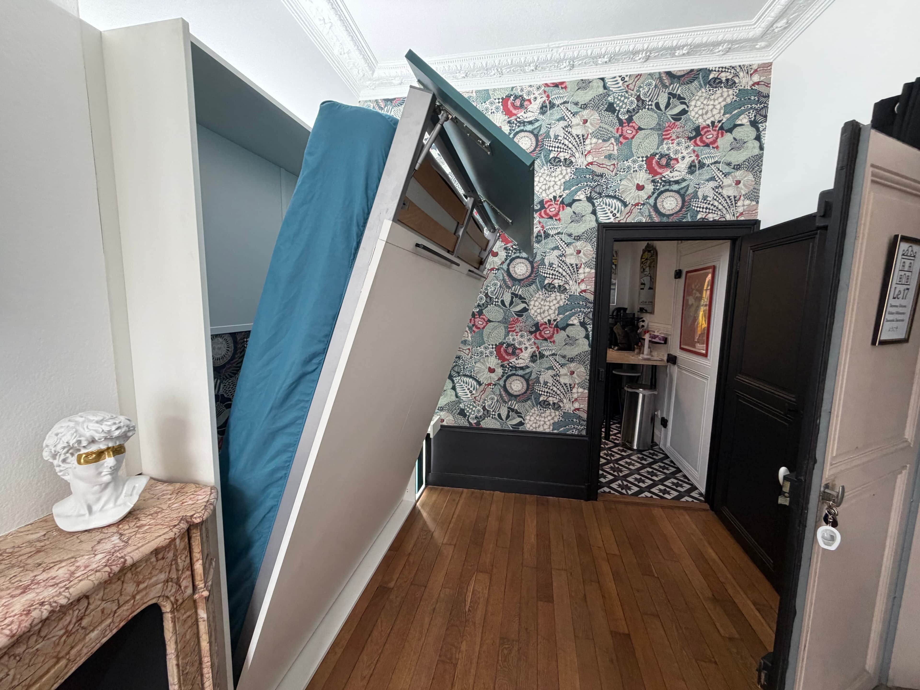 A room with a wooden floor, a blue curtain, a white bust sculpture, and a patterned wallpaper.