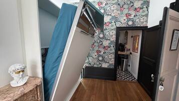 A room with a wooden floor, a blue curtain, a white bust sculpture, and a patterned wallpaper.