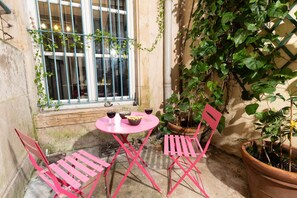 A small outdoor seating area with a pink table and chairs, a window with bars, and potted plants. - The 17th historic heart of Nancy (Nancy)