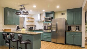 Une cuisine moderne avec des armoires de couleur turquoise, des appareils en acier inoxydable et un îlot central doté de tabourets de bar.
