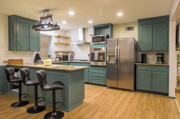 A modern kitchen with teal cabinets, stainless steel appliances, and a central island with bar stools.