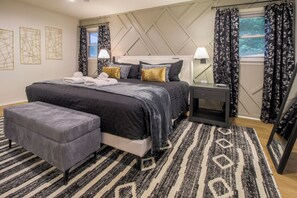 Une chambre à coucher moderne avec un grand lit, des tables de chevet, un banc et un tapis à motifs.