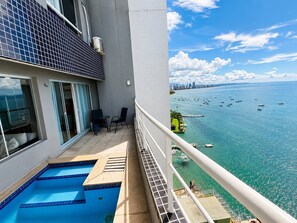 Un balcón con piscina, horizonte urbano y barcos en el agua.