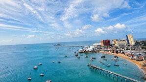 A coastal cityscape with a pier extending into the sea, numerous boats, and buildings along the shore. - Hosts BR - Cobertura duplex frente mar (Fortaleza)