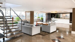A modern lobby with a staircase, seating area, reception desk, and a view of the outside. - Hosts BR - Cobertura duplex frente mar (Fortaleza)