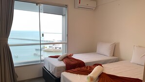 A hotel room with two beds, a window with a view of the sea and a bridge, and an air conditioning unit on the wall. - Hosts BR - Flat Vista Mar no Meireles (Fortaleza)