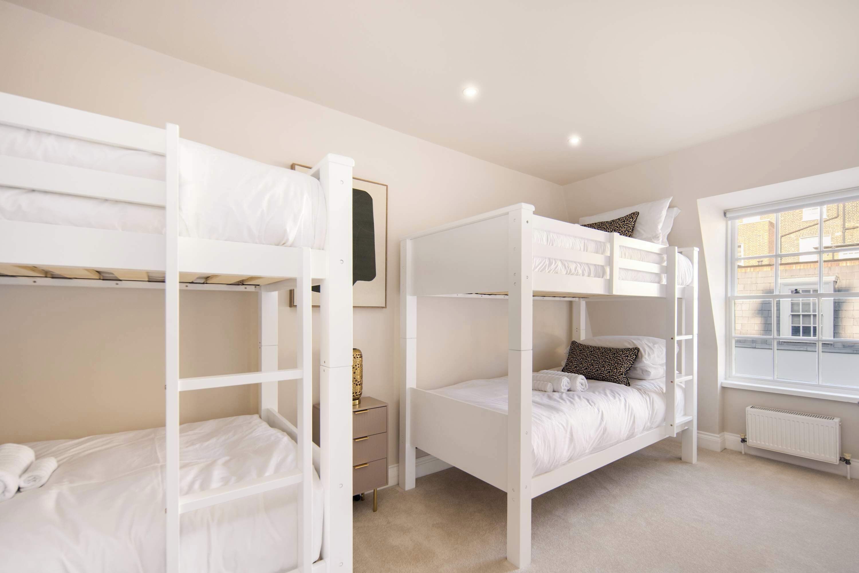 A room with bunk beds, a small bedside table, a radiator, and a window with a view.