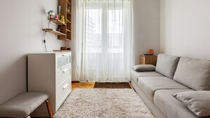 Een moderne woonkamer met een bank, een bijzettafeltje, een kast en een raam met transparante gordijnen.