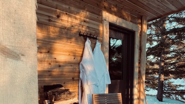 A wooden deck with a bench and a chair, a fireplace, and a coat rack with a white garment. - Smokey Hollow Motel & Resort (Onanole)