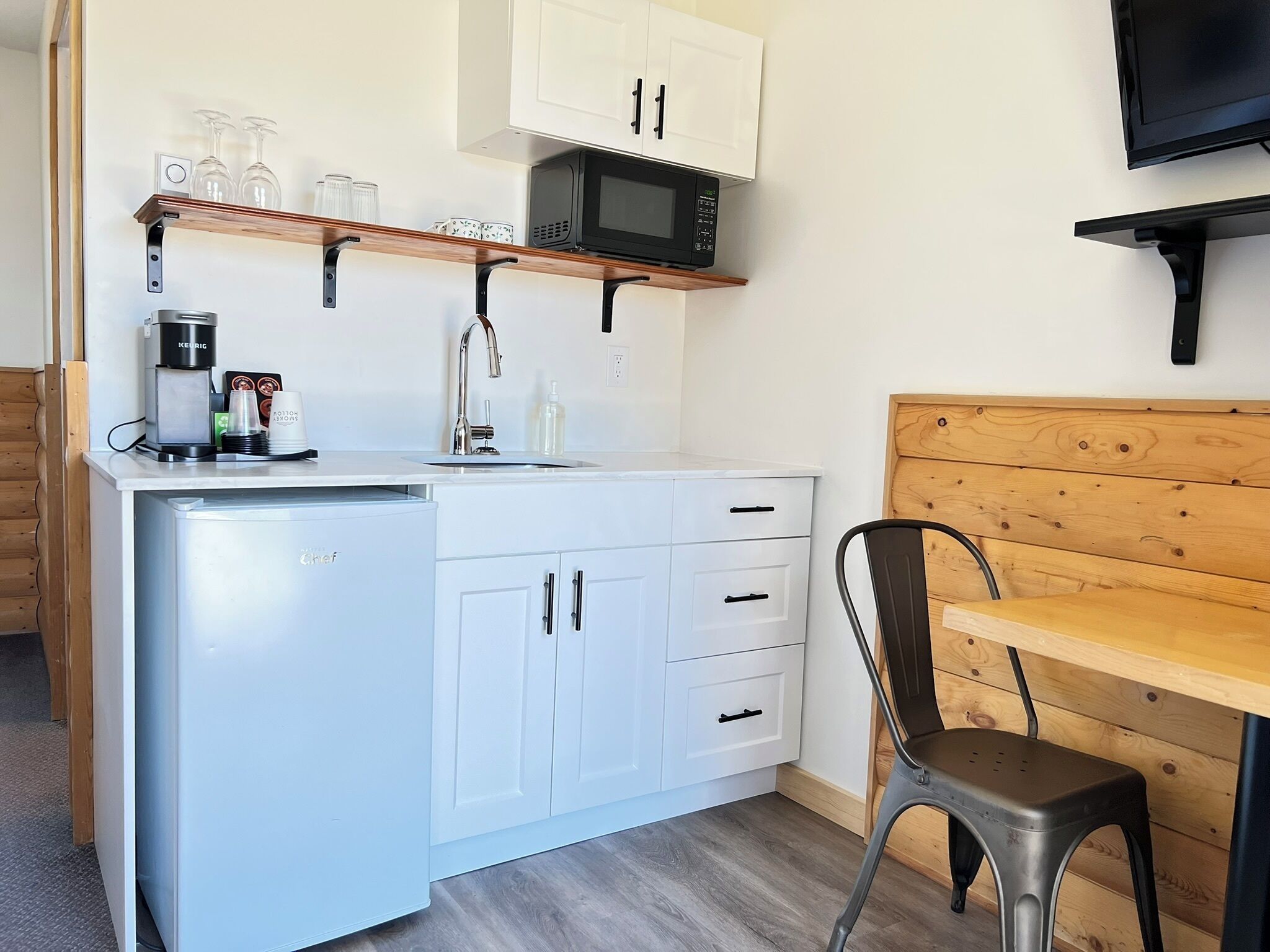 A compact kitchen with a refrigerator, microwave, and a wooden bench.