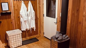 A wooden room with a sauna, a door, and two white towels hanging on hooks. - Smokey Hollow Motel & Resort (Onanole)