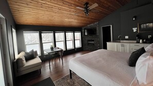 A bedroom with a large bed, a desk, a chair, a sofa, and a TV mounted on the wall. - Smokey Hollow Motel & Resort (Onanole)