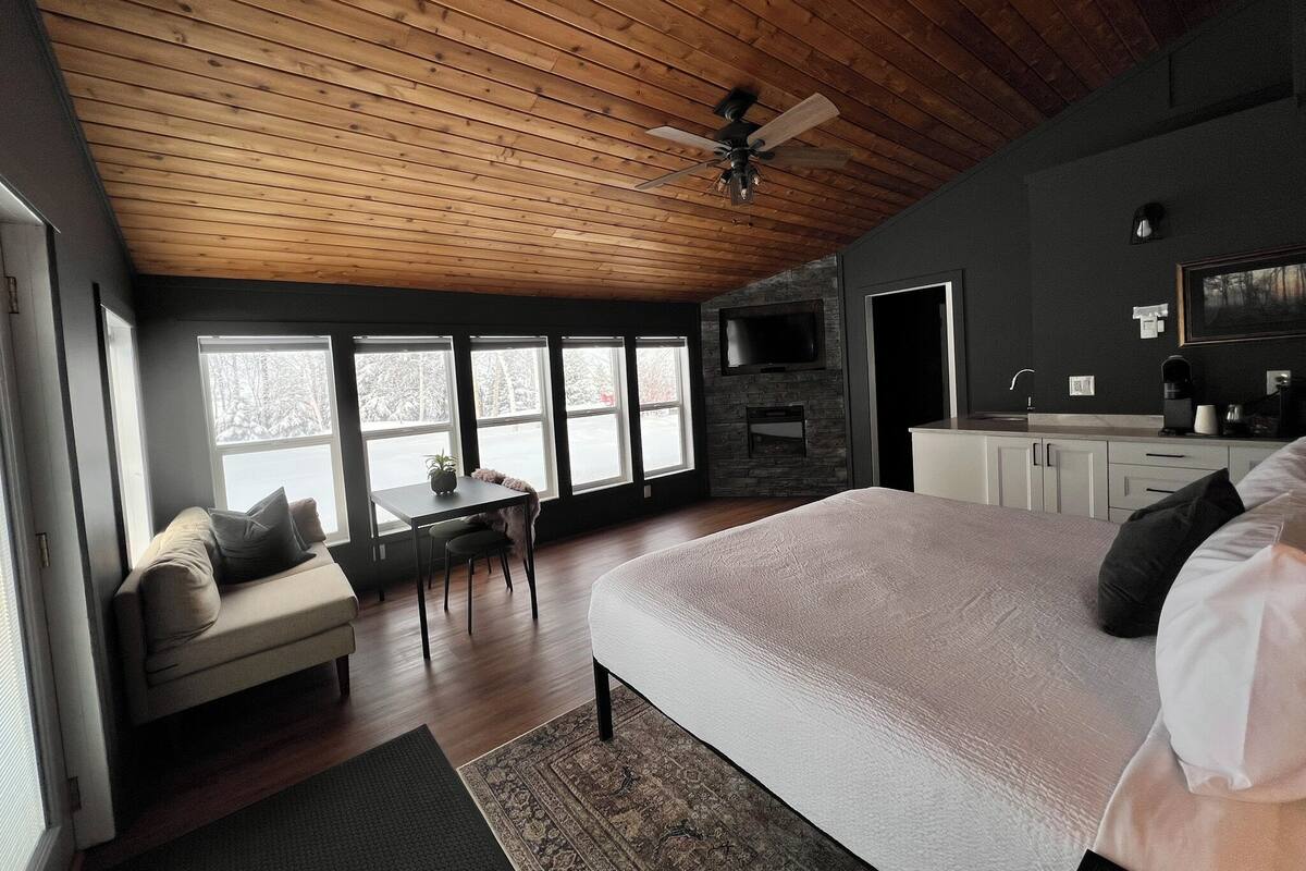 A bedroom with a large bed, a desk, a chair, a sofa, and a TV mounted on the wall.
