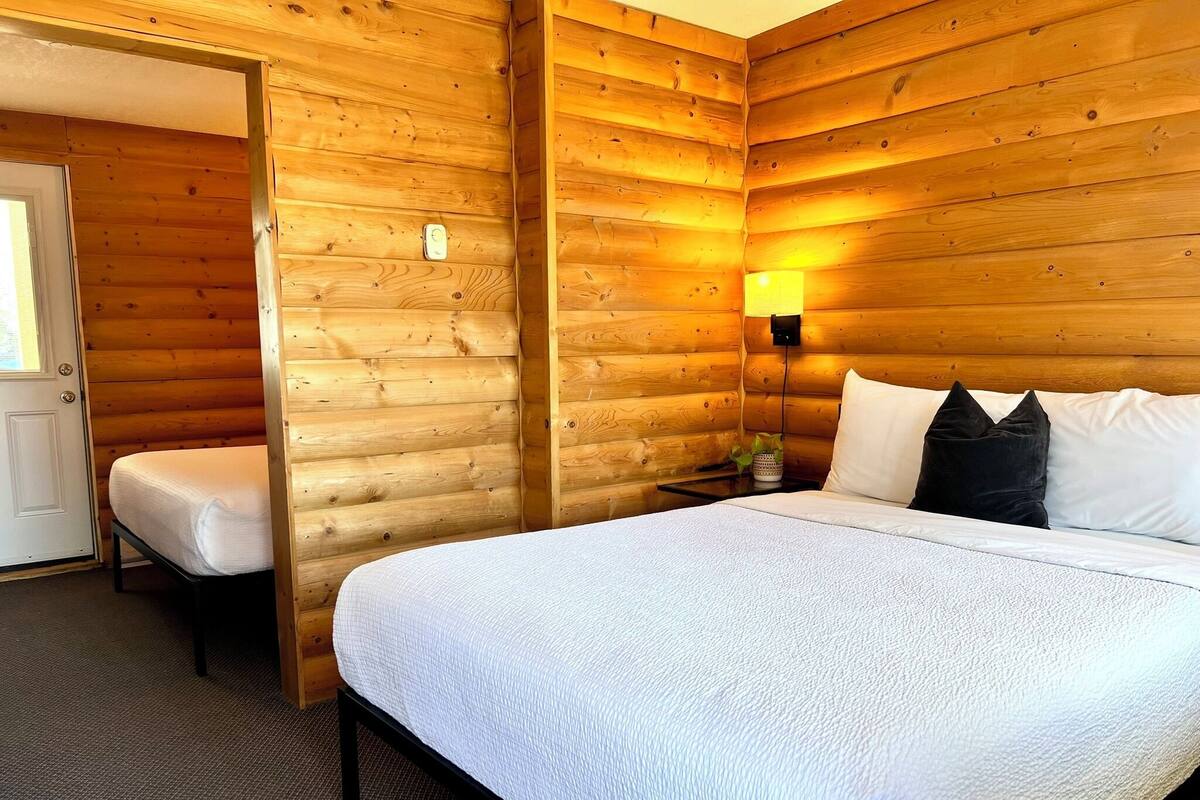 A wooden cabin room with a bed, bedside table, lamp, and a door.