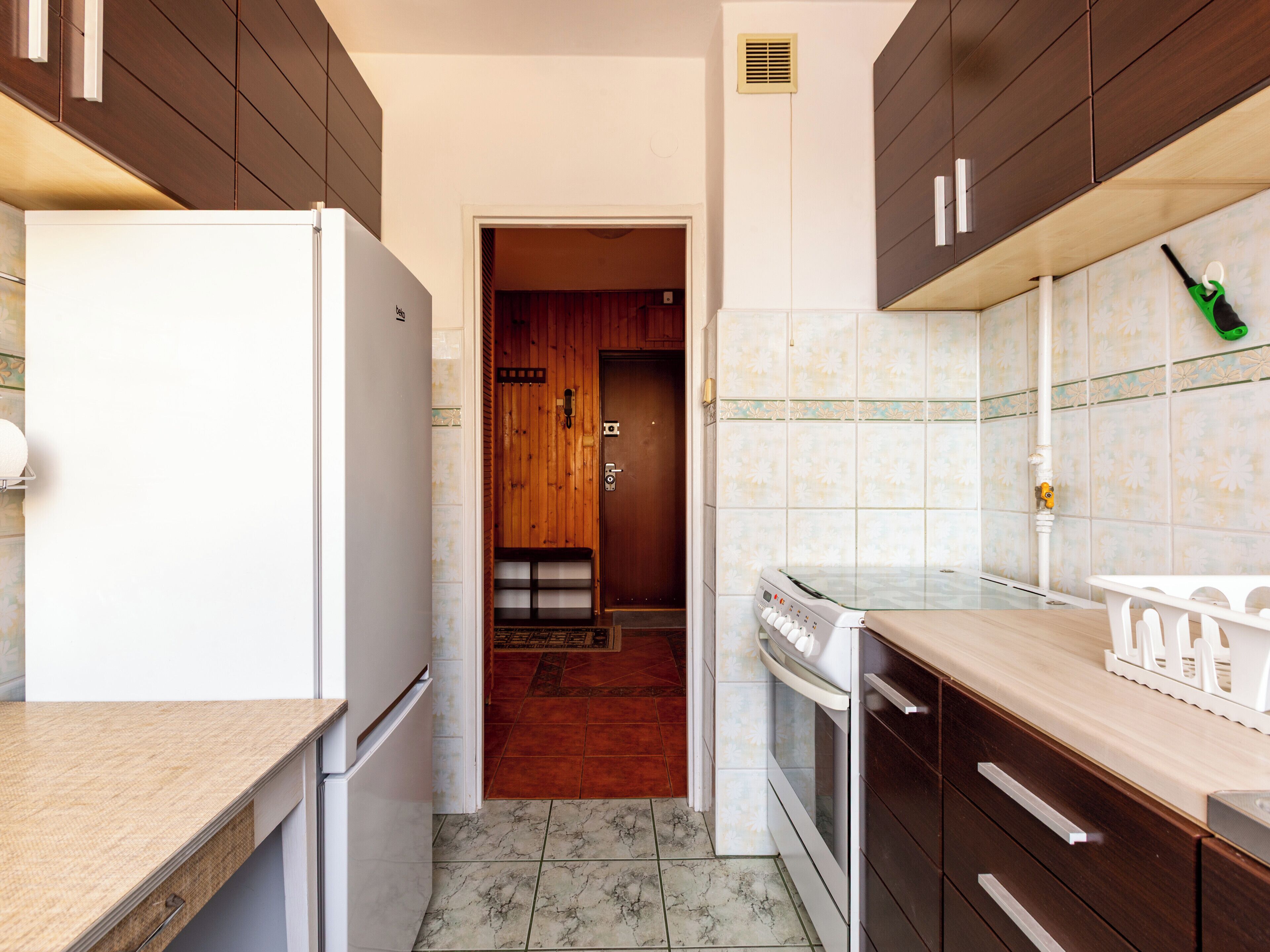 A kitchen with a refrigerator, oven, and cabinets. There is a door leading to another room.