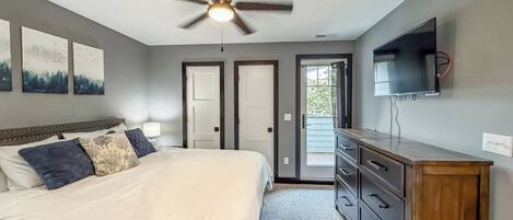 Une chambre à coucher comprenant un lit, un ventilateur de plafond, une commode, un téléviseur et deux portes.