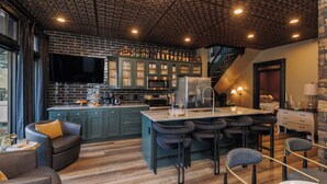 A modern kitchen with a central island, bar stools, and a dining area with a table and chairs. - *New* Speakeasy Highlands 7BR | Hot Tub | Sleep 14 (Louisville)