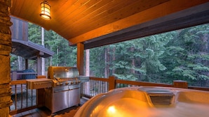 A wooden deck with a hot tub, grill, and a view of a forest. - Ski In Out Villa 464 I Private Hot Tub I Great Views I Outdoor Fireplace I Discounted Attractions (Winter Park)