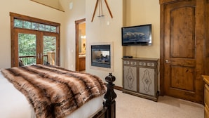 A bedroom with a large bed, a fireplace, a television, and a wooden door. - Ski In Out Villa 464 I Private Hot Tub I Great Views I Outdoor Fireplace I Discounted Attractions (Winter Park)