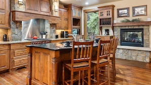 A kitchen with wooden cabinets, a stone fireplace, and a bar area with chairs. - Ski In Out Villa 464 I Private Hot Tub I Great Views I Outdoor Fireplace I Discounted Attractions (Winter Park)