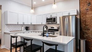 Een moderne keuken met witte kasten, roestvrijstalen apparatuur, een centraal eiland met barkrukken en hanglampen.