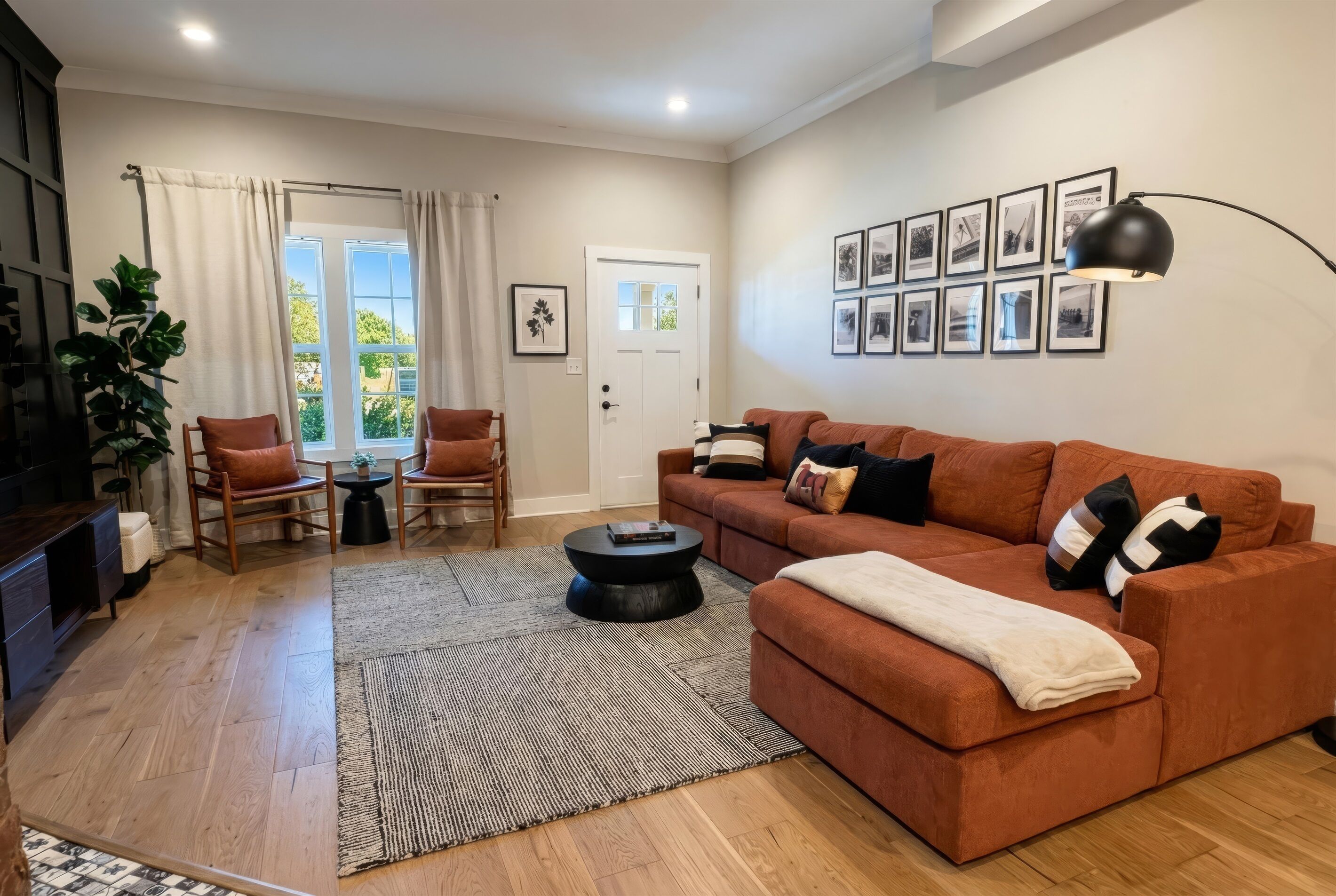 A living room with a brown sofa, a coffee table, and a TV. There are framed pictures on the wall, a plant, and a door with a window.