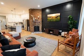 A modern living room with a fireplace, a large TV mounted on a dark wall, and a cozy seating area.