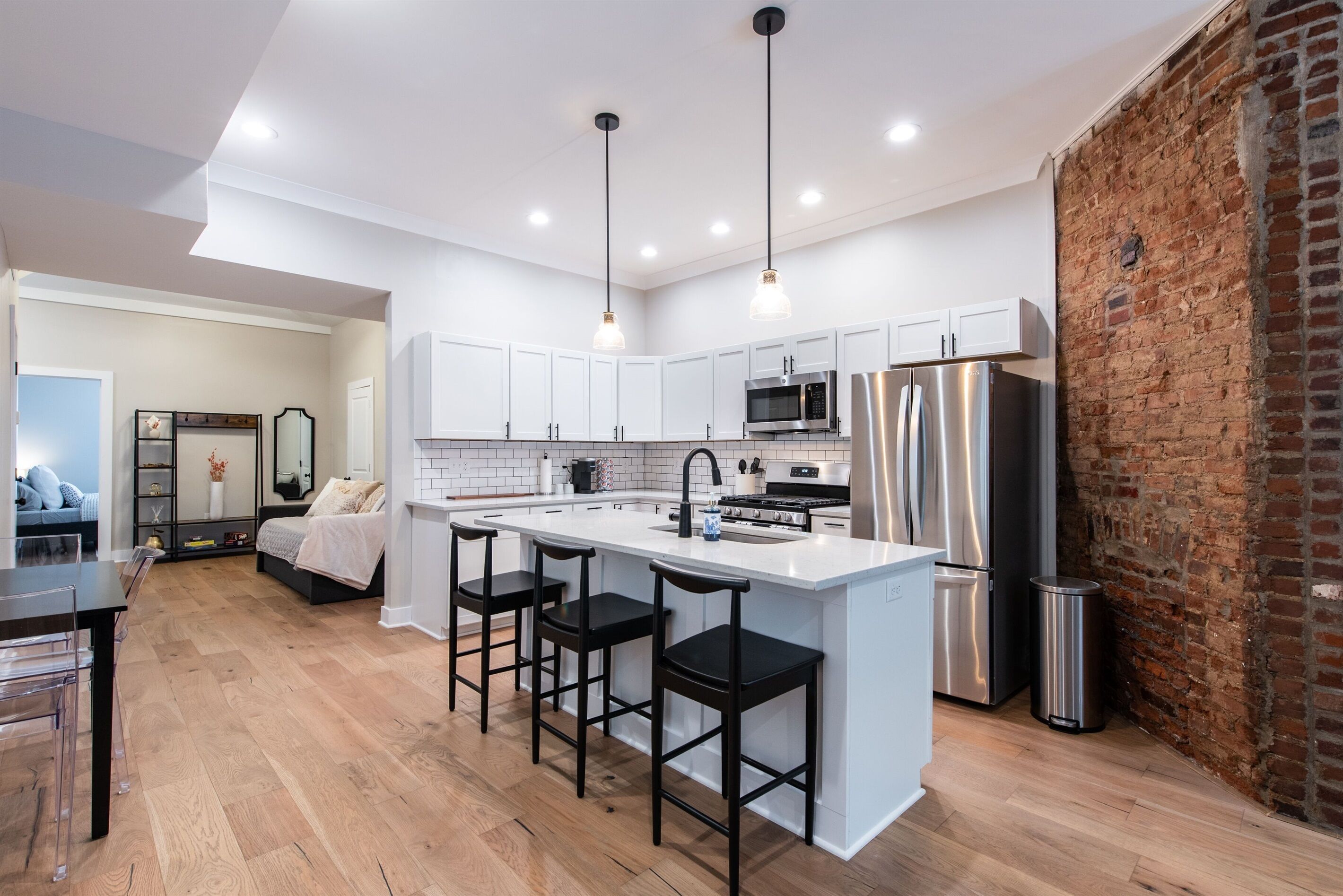 A modern kitchen with a central island, stainless steel appliances, and a brick wall.