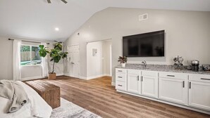 A modern kitchen with white cabinets, a large TV, and a countertop with various appliances and a plant. - Bourbon Trail Estate | 3 Epic Acres | 7 Bed 6 Bath (Louisville)