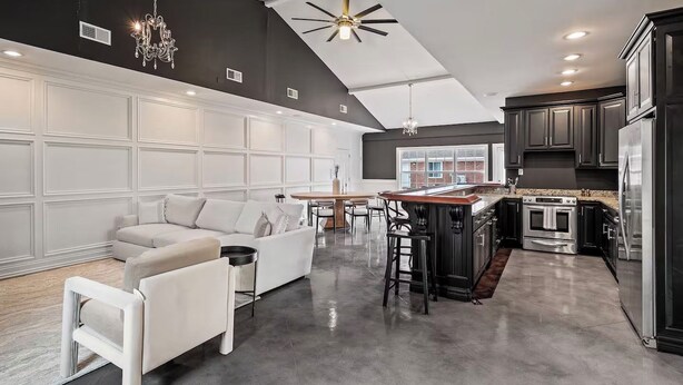 A modern kitchen with dark cabinetry, a central island, and a dining area with a white sofa and table. - Bourbon Trail Estate | 3 Epic Acres | 7 Bed 6 Bath (Louisville)