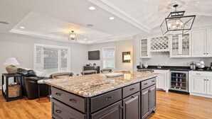 A modern kitchen with a large island, dark cabinetry, and a chandelier. - Bourbon Trail Estate | 3 Epic Acres | 7 Bed 6 Bath (Louisville)