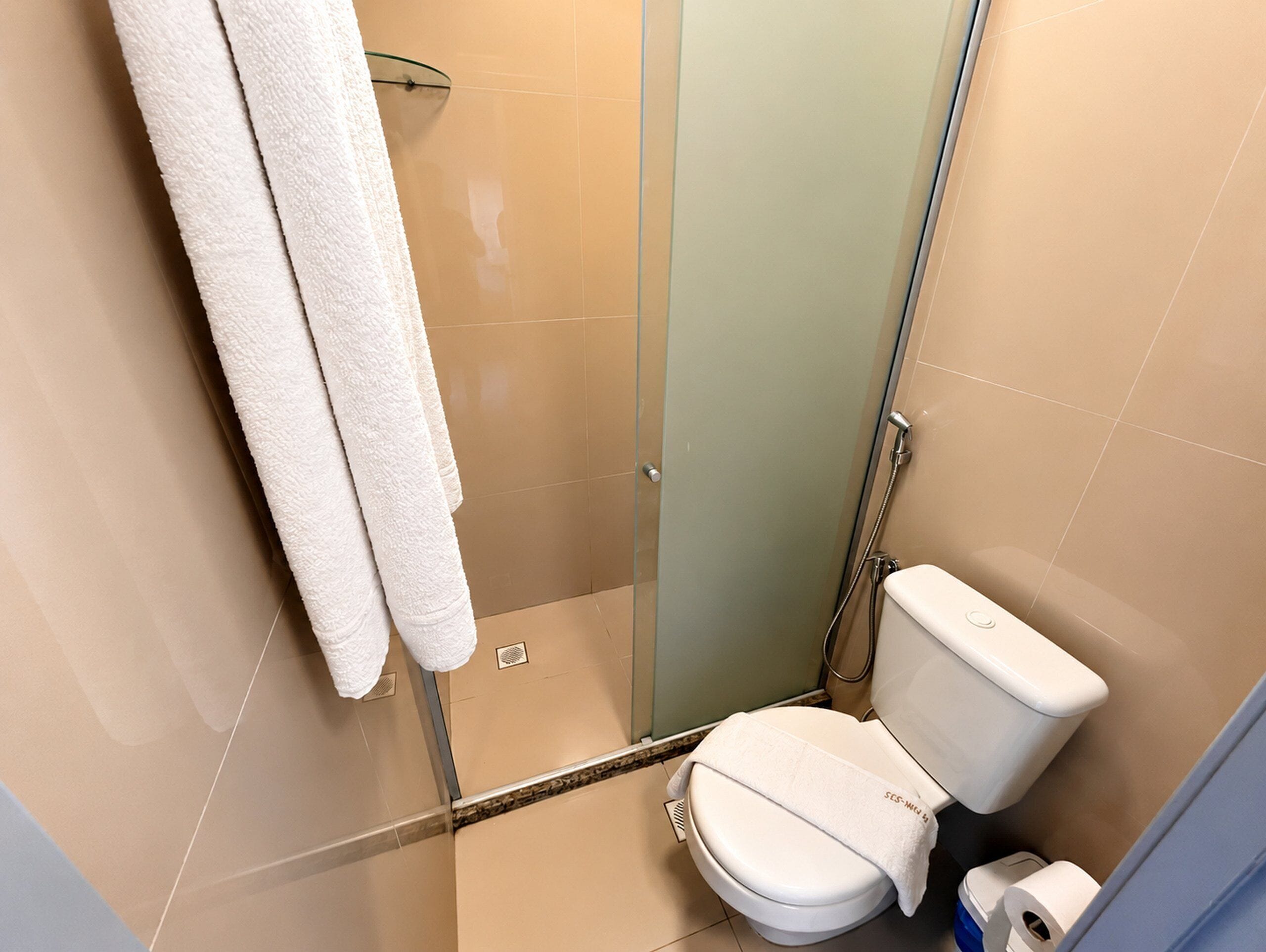Un baño con cabina de ducha de vidrio, inodoro y toallero con toallas.