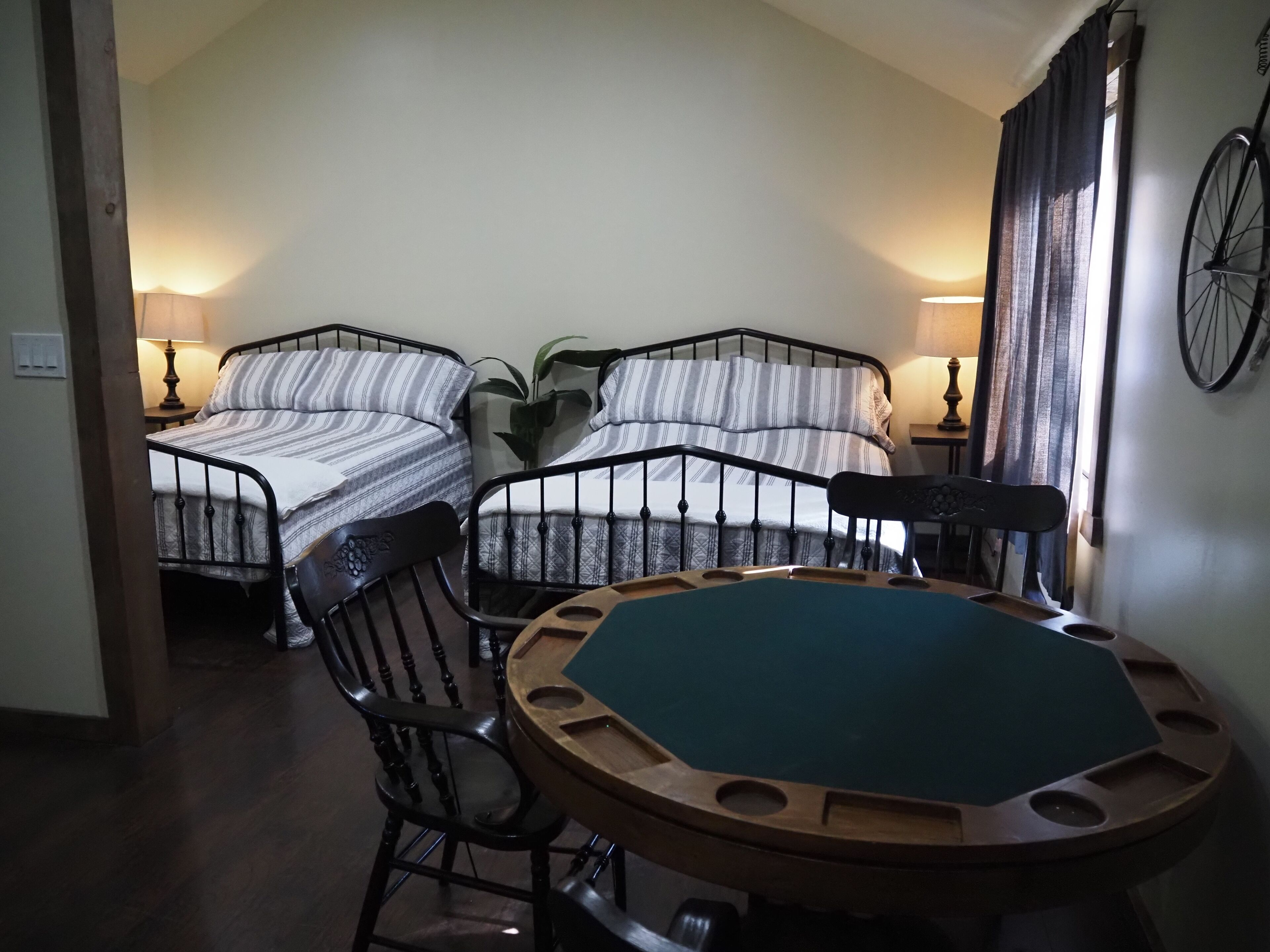 A room with two beds, a round table with chairs, a lamp, and a bicycle mounted on the wall.