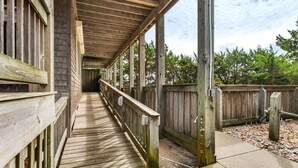 Une passerelle couverte en bois, dotée d’une rambarde en métal, mène à un bâtiment dont le mur est en briques.