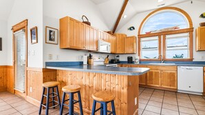 Une cuisine avec des meubles en bois, un plan de travail bleu et une grande fenêtre. On y trouve trois tabourets et un évier.