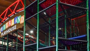 Una casita de juegos interior con un área de recreo delimitada por una malla verde y un letrero que dice "MEBERLAND PLAYHOUSE".