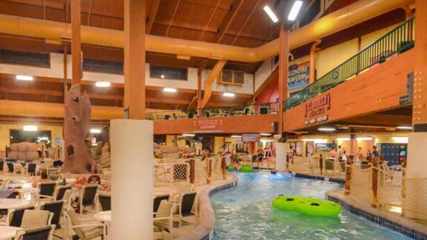 Una piscina interior con un flotador hinchable verde, sillas de descanso y un área de restaurante.