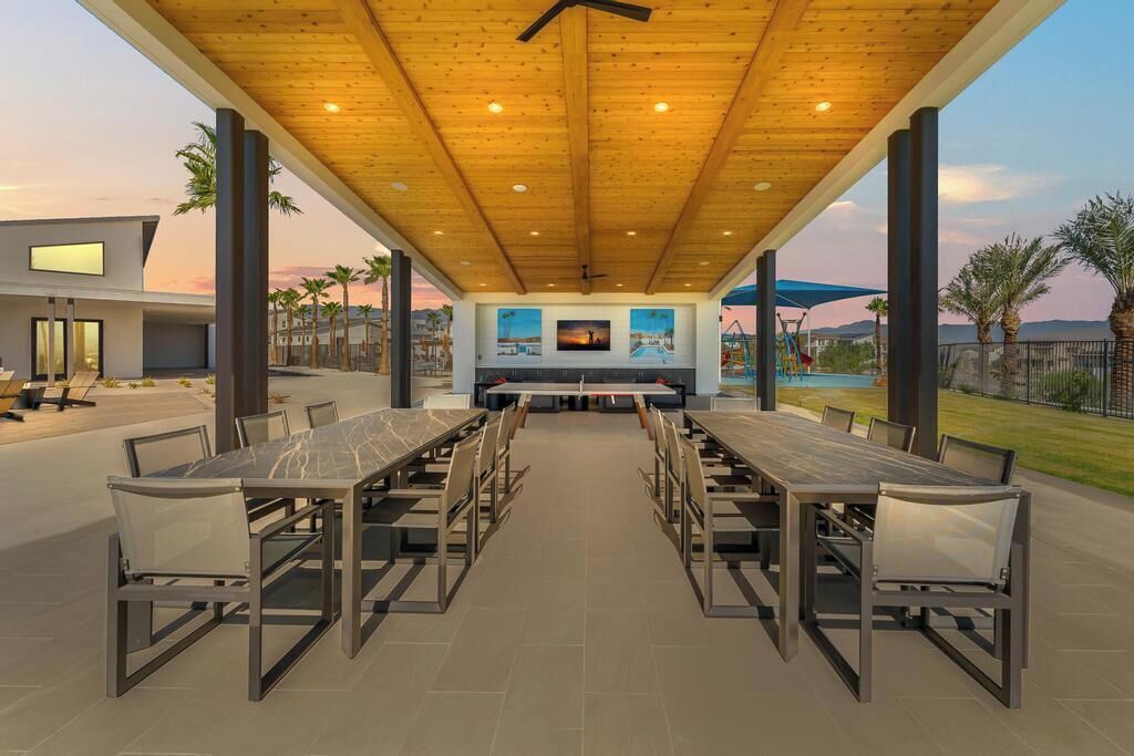 An outdoor patio with a long table and chairs, a ceiling fan, and a view of a pool and mountains.