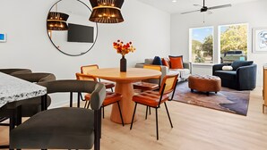 A modern living room with a round wooden table, orange chairs, a sofa, and a ceiling fan. - Sweet September - Stylish Waco Retreat in a Prime Location (Waco)