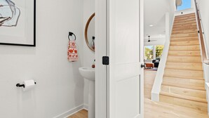 A modern bathroom with a toilet paper holder, a sink, and a mirror. - Sweet September - Stylish Waco Retreat in a Prime Location (Waco)