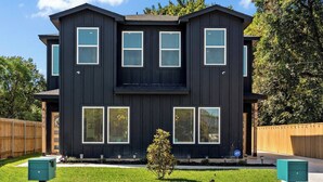 A two-story house with a dark exterior, multiple windows, and a small tree in the front yard. - Sweet September - Stylish Waco Retreat in a Prime Location (Waco)