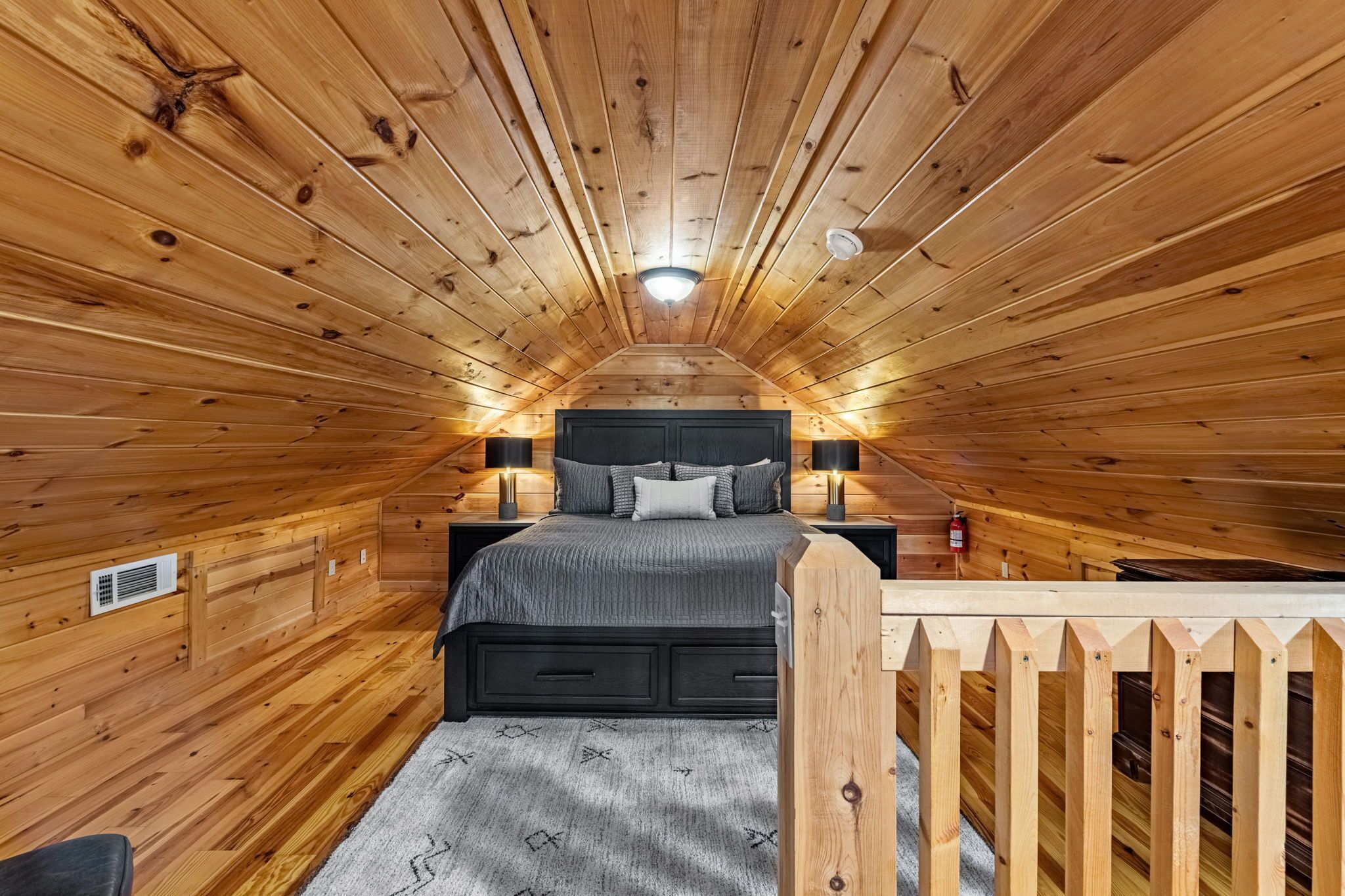 A wooden-paneled bedroom with a bed, nightstands, and a wooden railing.