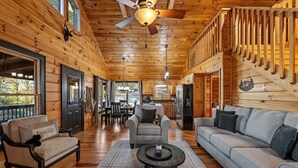 A cozy cabin interior with wooden walls, a dining area, and a living room with a sofa and armchairs. - Narcoossee Ridge -  NEW, Hot Tub, Views, Arcade and Airhockey (Mineral Bluff)