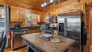 A wooden cabin kitchen with a central island, stainless steel appliances, and a window overlooking a forest. - Narcoossee Ridge -  NEW, Hot Tub, Views, Arcade and Airhockey (Mineral Bluff)