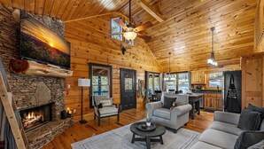 A cozy cabin interior with a stone fireplace, wooden walls, a dining area, and a living room with a sofa and coffee table. - Narcoossee Ridge -  NEW, Hot Tub, Views, Arcade and Airhockey (Mineral Bluff)