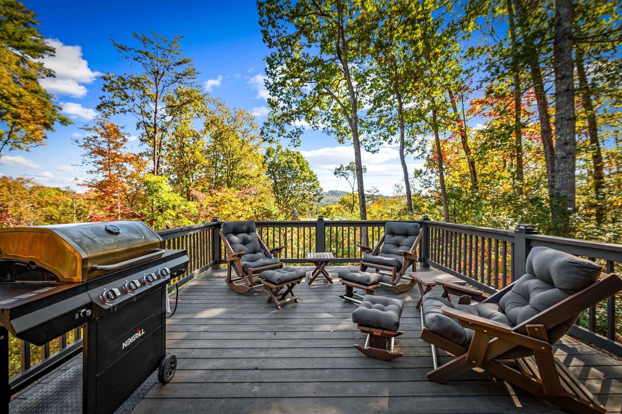 An outdoor deck with a grill, lounge chairs, and a view of trees.