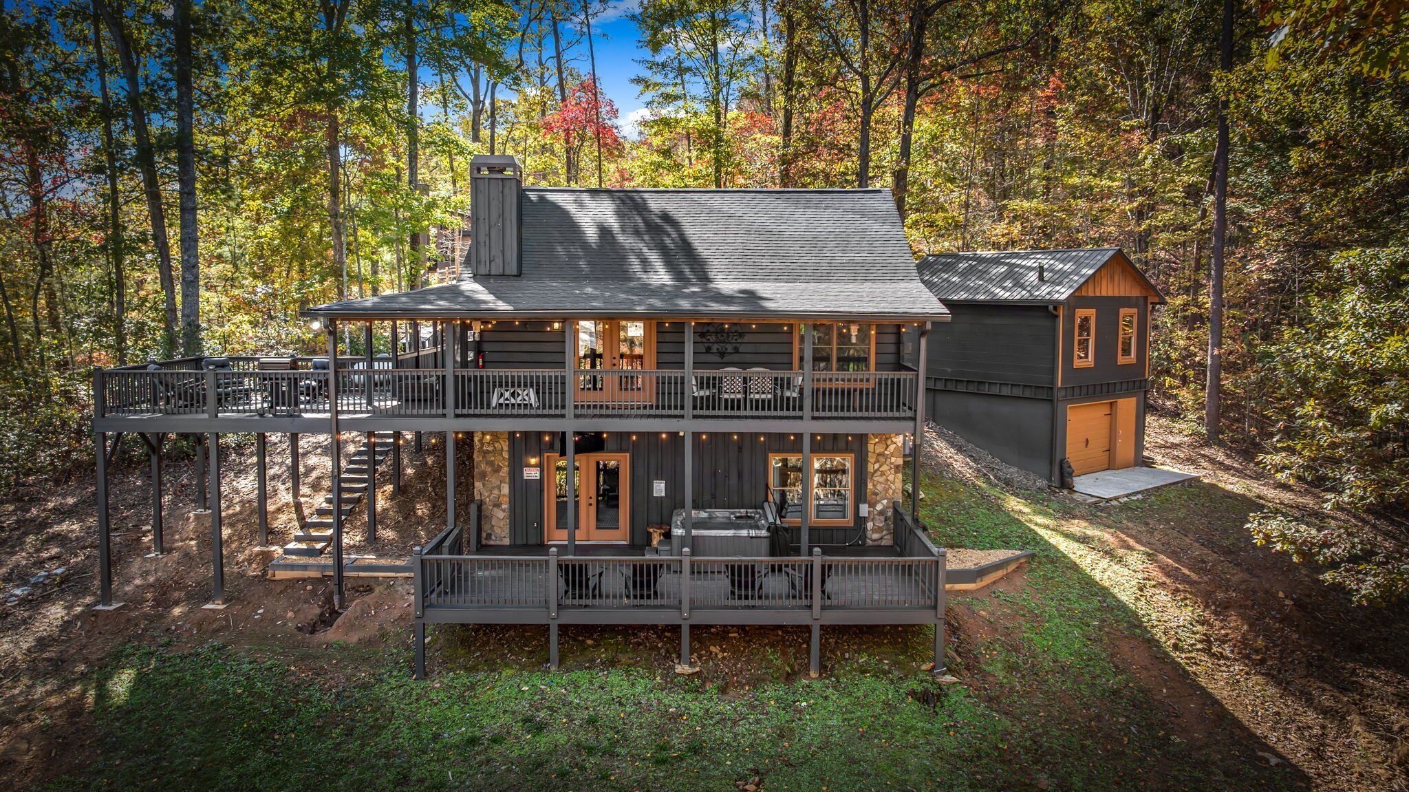 A two-story cabin with a balcony, a hot tub, and a separate garage.