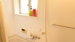 A small, white bathroom with a bathtub, a shower, and a window above the sink. - GINTAKEI (Osaka)